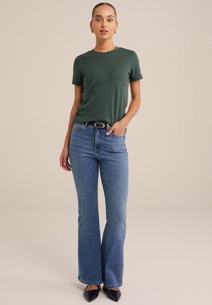 Mørkegrøn korte ærmer t-shirt kombineret med lyseblå flared jeans. Outfitet suppleres med et sort bælte og spidse sorte sko.