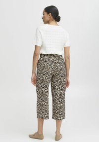 Bílý pletený krátký rukáv top kombinovaný s béžovými kalhotami s leopardím vzorem až po lýtka. Modelka má na sobě ploché hnědé boty; vlasy stylizované do nízkého drdolu.