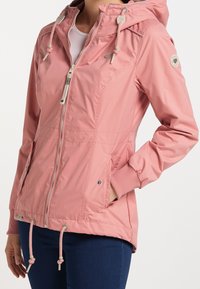 Lichtroze jack met een capuchon, ritssluiting, elastische manchetten en een trekkenkoord in de taille. Voorzien van zijzakken en een logo-opdruk op de mouw.