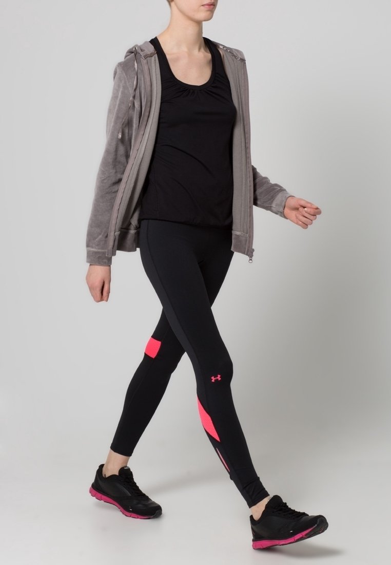 Persona che cammina indossando leggings sportivi neri con dettagli rosa, una canotta nera, una felpa grigia con zip e sneakers nere con suole rosa.