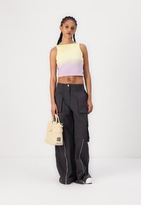 Crochet crop top in yellow to lavender gradient; loose-fitting dark cargo pants with zippers; beige bag with multiple pockets; casual sneakers.
