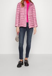 Rosa vadderad pufferjacka med hög krage och dragkedjefickor, i kombination med mörka smala jeans och kraftiga svarta loafers.