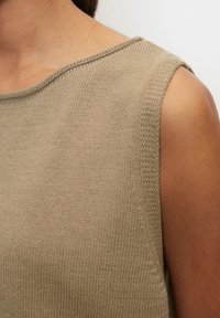 Sleeveless beige knitted top on person with medium skin tone, showing close-up of shoulder and neckline details.