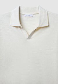 Polo shirt beige chiaro con scollatura a V, texture a coste e colletto. Presenta un'etichetta con il testo "CALLIOPE". Finitura del tessuto liscia.