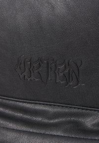 Material de piel sintética negra con letras en relieve. Textura suave con un patrón de grano visible y costuras a lo largo del borde inferior.