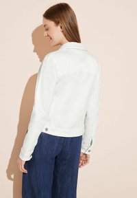 Weiße Jeansjacke mit klassischem Kragen, Knopfdetails und aufgesetztem Schnitt, kombiniert mit dunkelblauen weit geschnittenen Hosen.