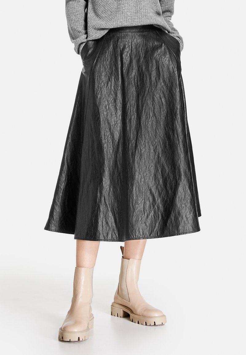 Svart, texturerad A-linjeformad kjol med midikalvlängd, som har fickor och en slät midjeband, matchad med ljusbeige ankelboots.