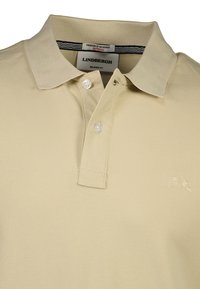 Beige polo skjorte med en afslappet pasform, der har krave, to knapper, struktureret stof og et lille broderet logo på brystet.