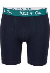 Mörkblå bomullskalsonger med en teal-elastisk midja som har vit logotext. Designade med en figurnära passform och släta sömmar.