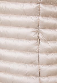 Jasny beżowy puchowy kurtka z poziomymi pikowanymi panelami, gładkim satynowym wykończeniem i małym zapięciem na zamek z przodu.