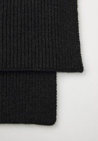 Musta ribade tekstilkangas pehme ja tekstuurse pinnaga, millel on vertikaalsed mustrid ja puhtad servad, näidates kahte kattuvat tükki.