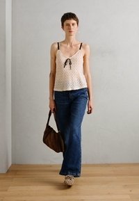 Camisola in pizzo floreale di colore rosa chiaro, abbinata a jeans a zampa d'elefante blu a vita alta. Accessoriata con una borsa marrone e tacchi con motivo.