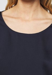 Haut marine à la texture lisse et à l'encolure large et arrondie, souligné par une couture discrète le long du bord. Design minimaliste.