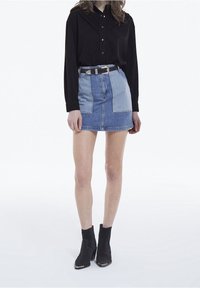 Farkkuhame, jossa on tilkkutyökuvio, koostuu vaaleansinisistä ja tummansinisistä paneeleista; yhdistetty mustaan pitkähihaiseen paitaan ja mustiin nilkkureihin.