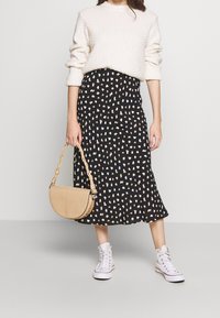 Black skirt with cream and brown abstract spots, paired with a textured cream sweater and white sneakers. Beige croc-embossed handbag.
