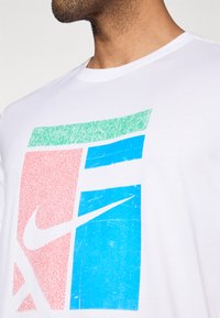 Balts kokvilnas T-krekls ar daudzkrāsainu grafiku sarkanā, zaļā un zilā krāsā, ar izteiktu Nike logotipu baltā krāsā.