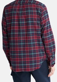 Camicia di flanella a quadri rossa e blu navy, maniche lunghe, polsini con bottoni, con orlo curvo e dettaglio della cucitura del giromanica posteriore. Tessuto morbido.