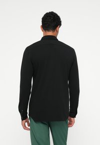 Maglietta nera a maniche lunghe con colletto, caratterizzata da polsini con bottone e orlo sagomato. Tessuto liscio, design semplice, senza motivi.