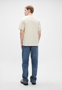 Μπεζ κοντομάνικο μπλουζάκι με ίσια γραμμή, συνδυασμένο με μπλε τζιν. Το σύνολο διαθέτει απλό σχέδιο και ουδέτερη παλέτα χρωμάτων.