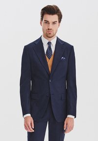Granatowy garnitur o dopasowanym kroju, z dwiema guzikami, klapami typu notch oraz teksturowaną poszetką. Biała koszula i wzorzysta krawat.