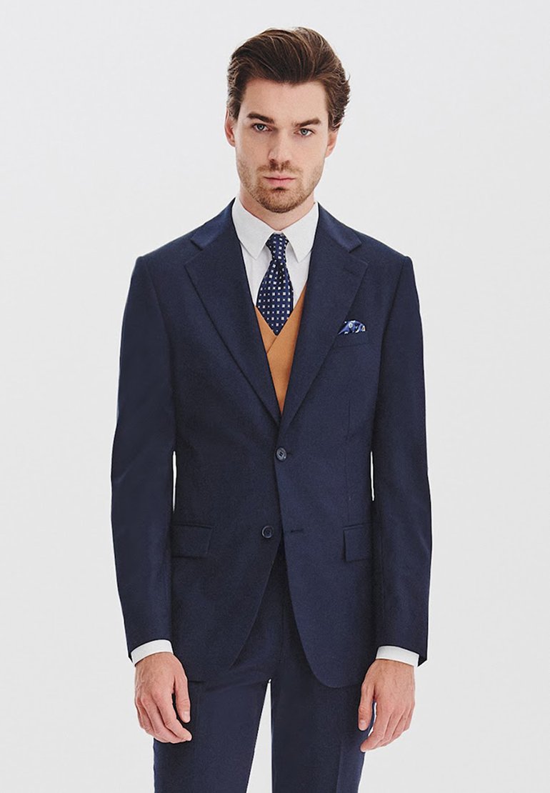 Granatowy garnitur o dopasowanym kroju, z dwiema guzikami, klapami typu notch oraz teksturowaną poszetką. Biała koszula i wzorzysta krawat.