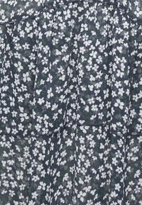 Tessuto da abito navy con motivo floreale caratterizzato da fiori bianchi e piccole foglie verdi. Leggero, semi-trasparente con design a strati.