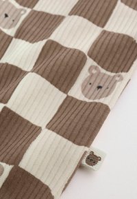 Soft knitted fabric with a brown and cream checkerboard pattern featuring repeated bear faces and a small bear tag.