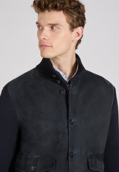 Ciemna zamszowa kurtka z dzianinowym kołnierzem, posiadająca dwie przednie kieszenie, zapięcie na guziki oraz teksturowane rękawy dla kontrastu.