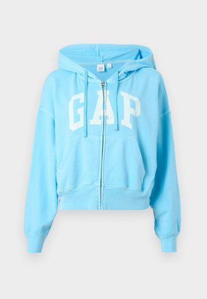 Sweat à capuche zippé bleu clair avec poches avant, capuche à cordon de serrage et grand logo "GAP" blanc sur la poitrine.