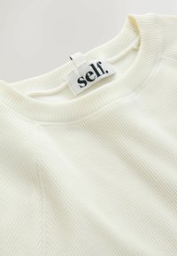 Ribakujuline kreemikaalune sweatshirt ümmarguse dekolteega ja seljas kangast silt, millel on kiri "self." Pehme tekstuur ja lihtne disain.