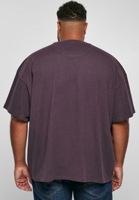 Tricou oversized de culoare mov, cu mâneci scurte, realizat din material de bumbac. Dispune de un gât rotund și un design simplu pe spate, fără detalii suplimentare.