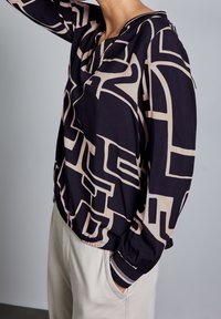 Mönstrad blus i svart och krämfärg med en avslappnad passform, rundad halsringning, elastiskt nederkant och ärmslut. Mönstret har djärva, abstrakta former.