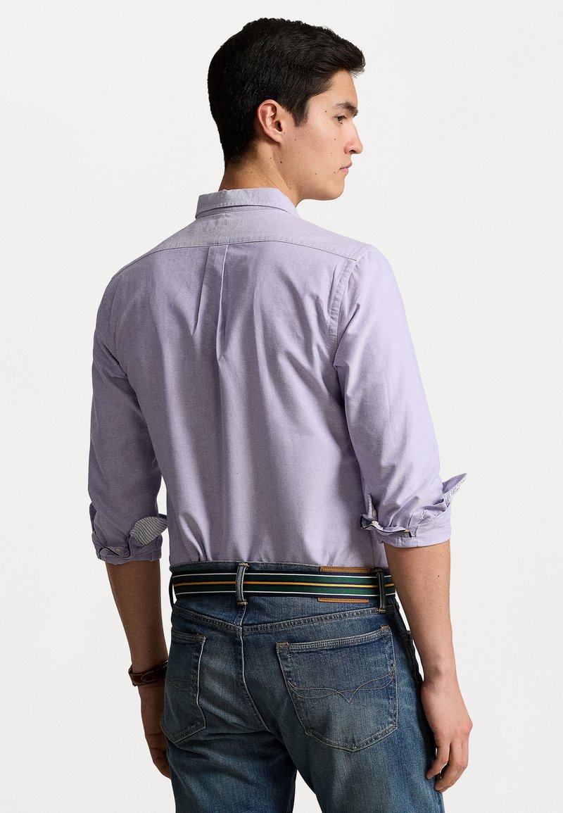 Paarse button-up shirt met opgerolde mouwen, textuurstof, rugplooidetail, gecombineerd met donkerblauwe jeans en een veelkleurige gestreepte riem.