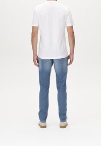 Bílé tričko s krátkým rukávem a kulatým výstřihem, doplněné světlými modrými džíny s dvěma zadními kapsami a obuví s béžovou podrážkou.