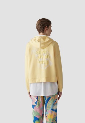 Yellow oversized hoodie with a hood, featuring embossed text "SHINE ON MY MIND" and a subtle floral pattern on the back.