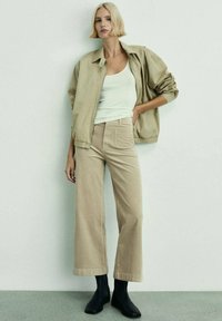 Beige cotton jacket over a white tank top, paired with beige wide-leg trousers and black ankle boots. Smooth textures, casual design.
