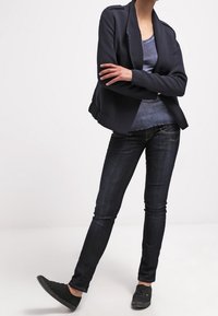 Blazer navy, blusa gris, jeans oscuros ajustados y zapatillas negras. El blazer tiene un diseño estructurado; los jeans son ajustados con un ligero desvanecimiento.