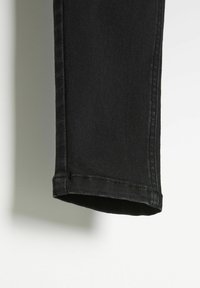 Czarne dżinsy o prostym kroju, z eleganckim dołem, subtelnymi detalami przeszyć i miękką teksturą.