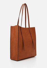 Sac fourre-tout en cuir marron avec de longues anses, de forme rectangulaire, au design minimaliste, et avec des coutures noires contrastantes le long des bords.
