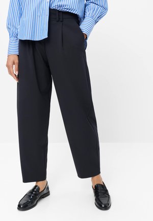 Personne portant un pantalon large noir raccourci, des mocassins noirs en cuir et une chemise rayée bleue et blanche avec les manches baissées.