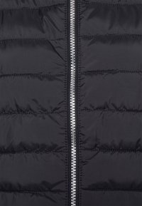 Czarna pikowana tkanina z poziomymi przeszyciami i centralnym suwakiem ze srebrnego metalu, ukazująca teksturę i szczegóły z bliska.