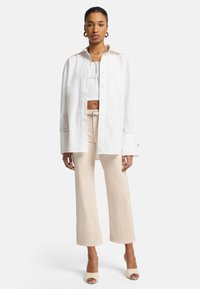 Chemise blanche surdimensionnée à boutons, pantalon beige court et escarpins nude. Tissu lisse, coupe décontractée et manches longues avec détails aux poignets.