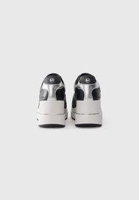 Schwarz und silberne Plateausneaker mit weißen, massiven Sohlen, von hinten gezeigt, mit einem kleinen runden Logo auf der Ferse.