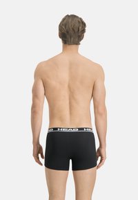 Boxers en coton noir avec une ceinture logo, vus de l'arrière. Texture lisse, design ajusté et taille mi-haute.