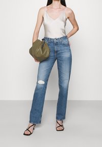 Světlá šedá saténová top, modré džíny s vysokým pasem s roztrhnutím, černé sandály na řemínky a zelená m ěkká taška.