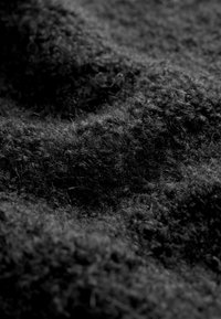 Close-up van donker, gestructureerd wolweefsel met dikke, donzige vezels en een zachte, onregelmatige oppervlakte met schaduwen van natuurlijk licht.