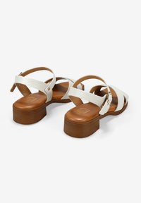 Sandalias de cuero blanco con tiras entrecruzadas y cierre de hebilla, que cuentan con una suela de plataforma marrón, textura suave y diseño minimalista.