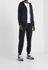 Navy hoodie med logodetaljer, matchande joggers och färgglada sneakers. Mjukt material, dragkedja och fickor på hoodien.