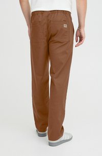 Brune bomullsbukser med elastisk midje, to baklommer og et merke. Benene er rett-snittet. Kombinert med grå og hvite joggesko.