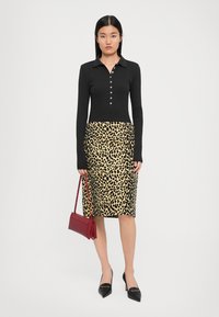 O bluză neagră cu mâneci lungi și nasturi, purtată împreună cu o fustă tip creion cu imprimeu de leopard. Modelul poartă o geantă roșie și tocuri negre cu vârf ascuțit.
